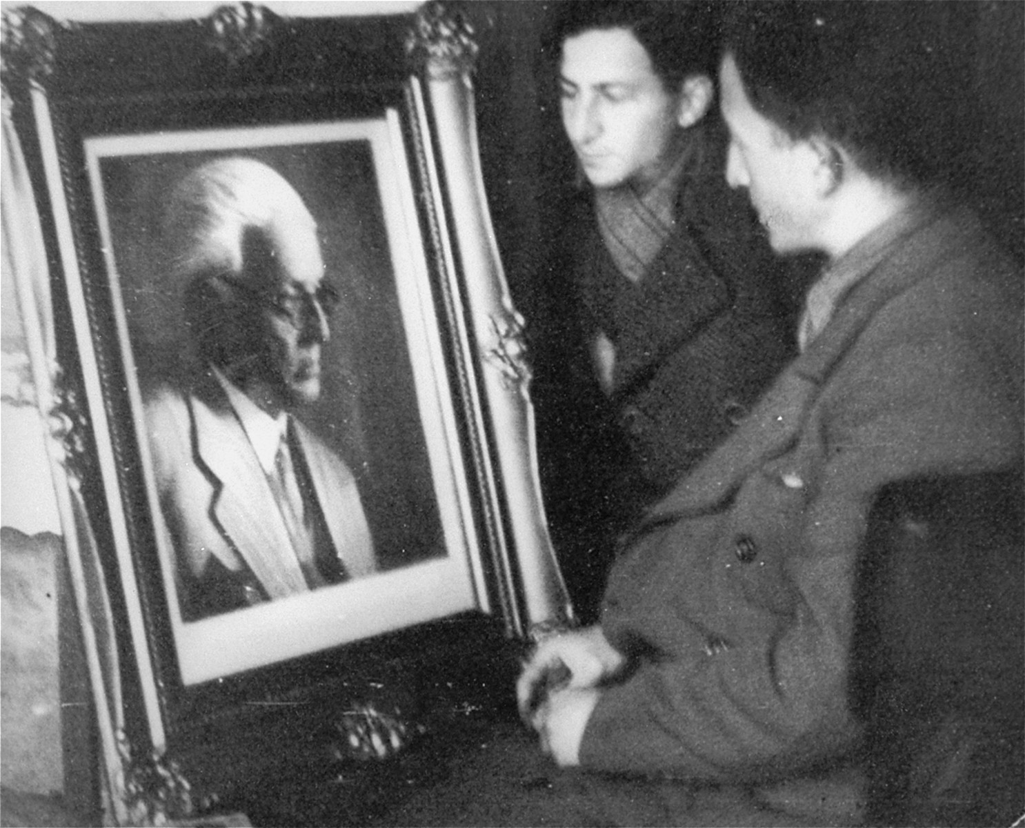 Nachman Zonabend (center) and Mendel Grosman (right) examine a framed portrait of Jewish Council chairman Mordechai Chaim Rumkowski.  

The portrait was photographed by Mendel Grosman and had to be displayed in every office in the Lodz ghetto. The original framed portrait was given to Rumkowski.