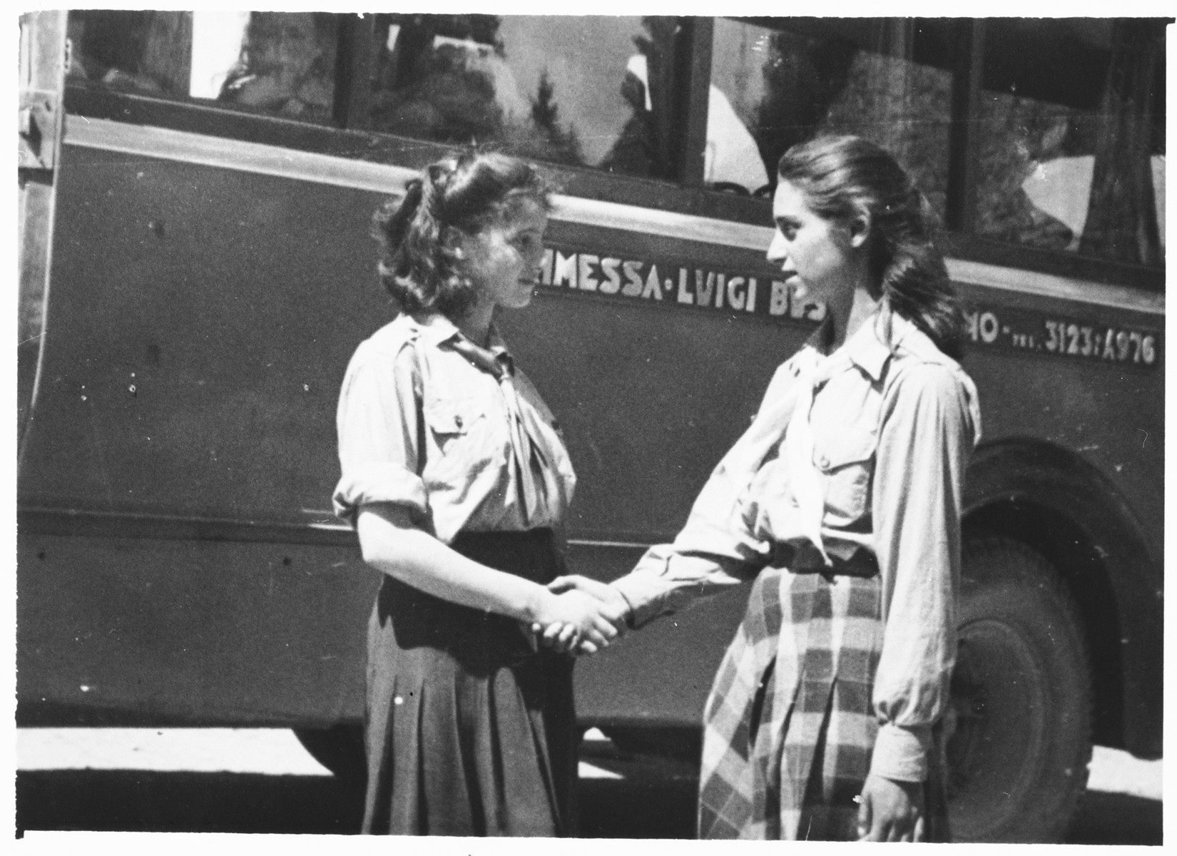 Two teenage girls shake hands in front of a bus outside the Selvino children's home.