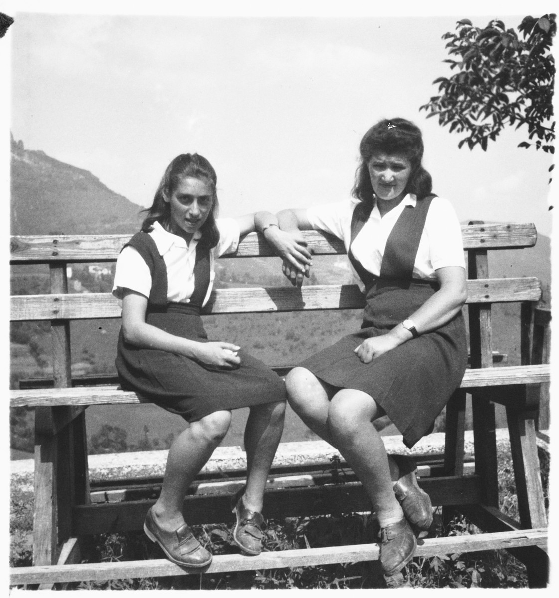 Two teenage girls sit on a wooden bench on the grounds outside the Selvino children's home.

Ruth Rotenburg is pictured on the left.