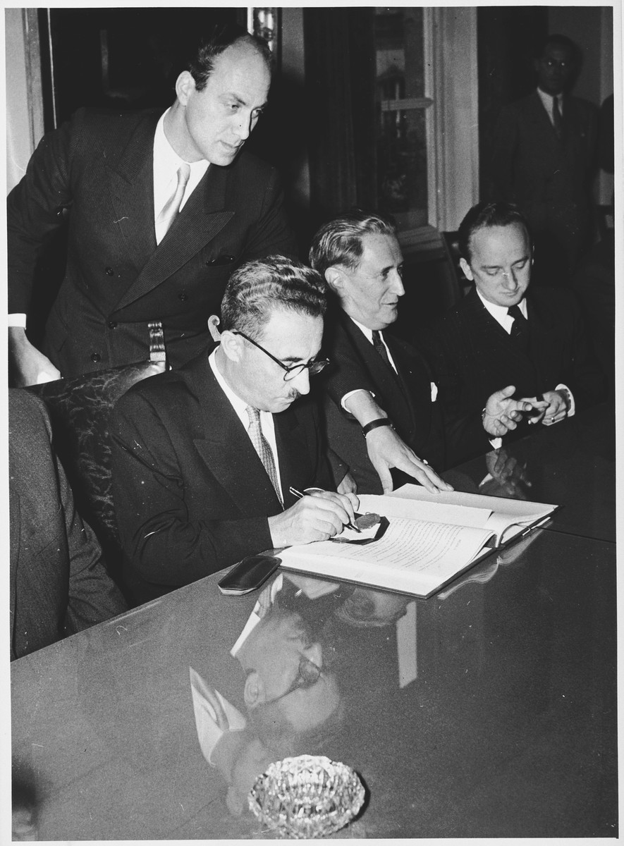 Israeli Foreign Minister Moshe Sharett signs the Reparations Agreement between the German Federal Republic, the State of Israel, and the Conference on Jewish Material Claims.  

Seated from left to right are: Felix Shinnar, Giora Josephthal, Moshe Sharett, Nahum Goldmann, and Benjamin Ferencz.