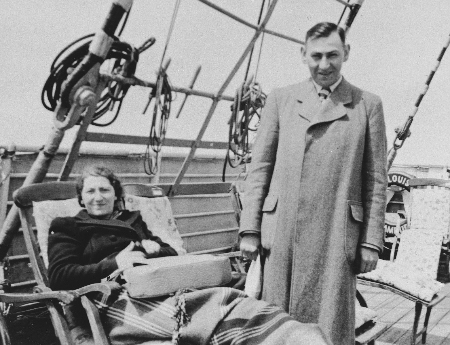 A female Jewish refugee relaxes on a deck chair while her husband stands next to her on the upper deck of the St. Louis.

Pictured are Ilse and Kurt Marcus.