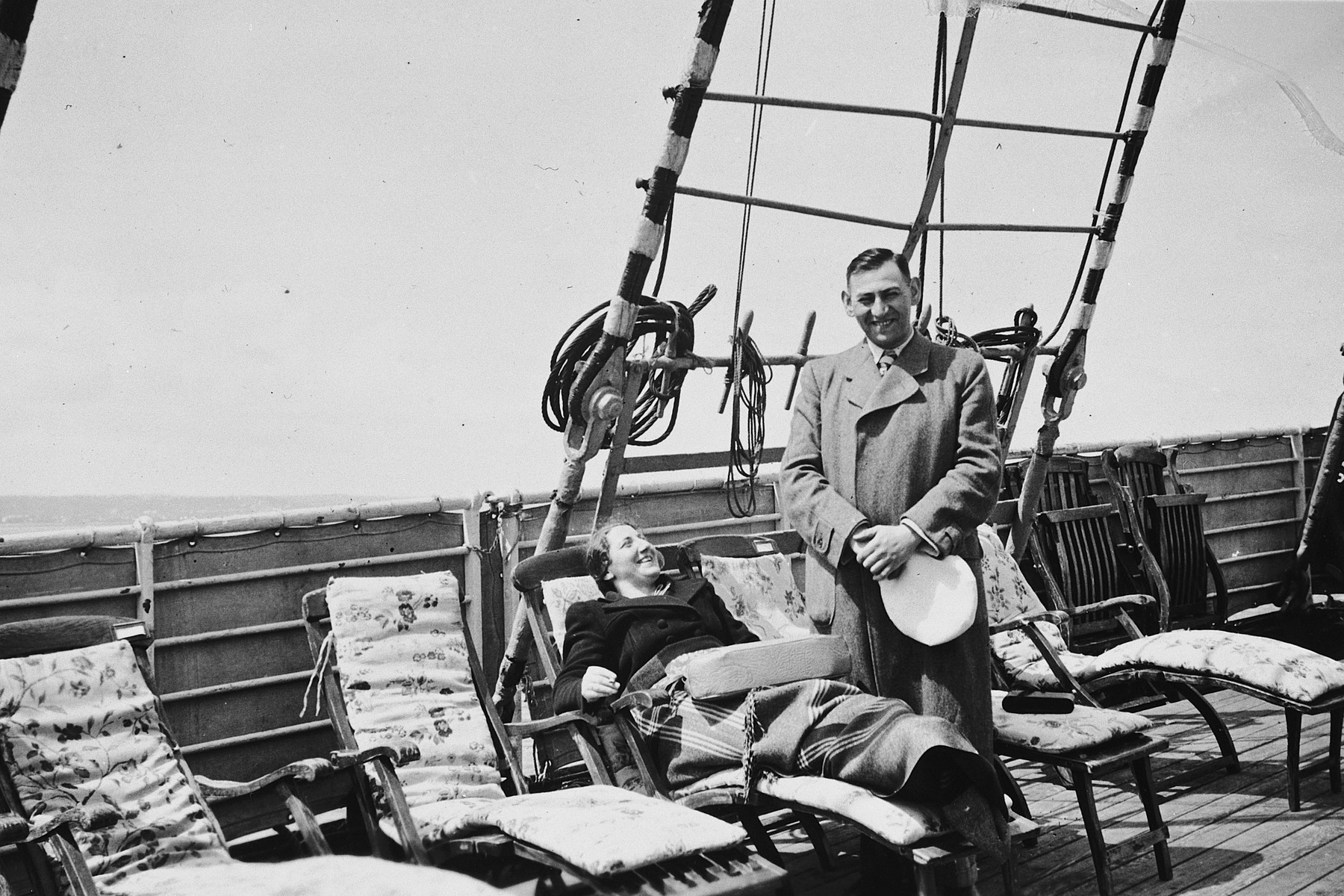 A female Jewish refugee relaxes on a deck chair while her husband stands next to her on the upper deck of the St. Louis.

Pictured are Ilse and Kurt Marcus.