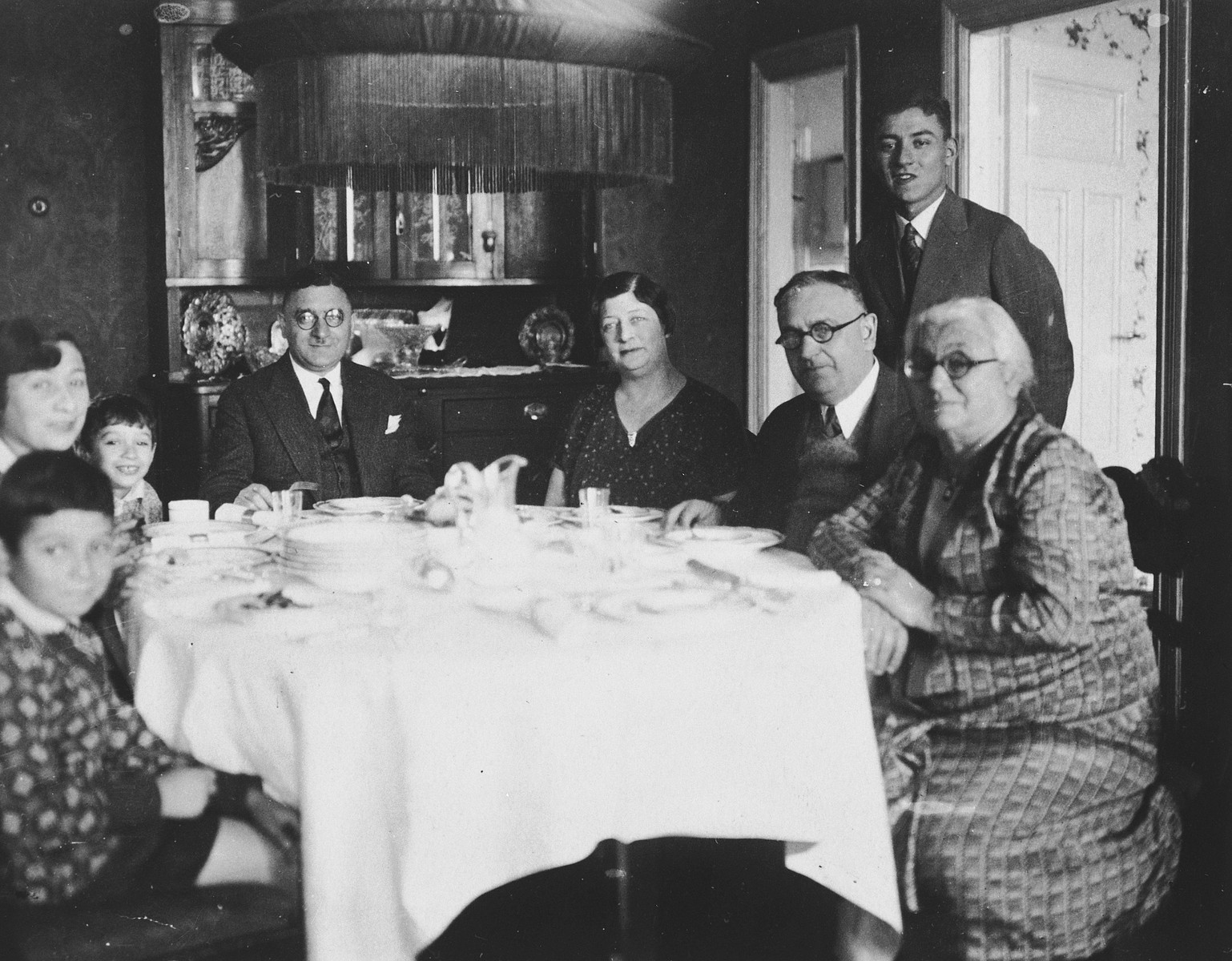 A Lithuanian Jewish family gathers around their dining room family.

Dr. Elias Sedlis sits at the head of the table.  To his right are his wife Anna and two sons, Alexander and Gabriel.  To his left is his sister Miriam, her husband, and his mother Shayne.  David Cukierman is standing.