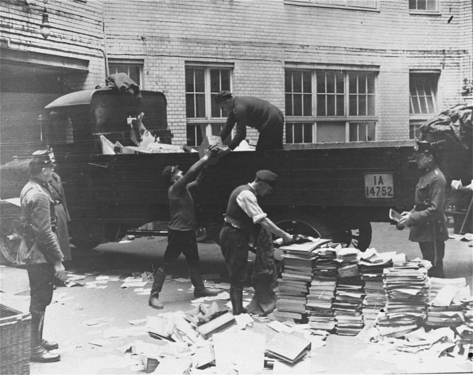 Civilians load Communist publications onto the back of a truck as police look on during a raid of the Karl-Liebknecht House (KPD headquarters), which was on the Buelowplatz in Berlin.  

The closing of Communist Party offices was declared necessary for the protection of the state in the Enabling Act, passed by the Reichstag soon after the fire of 28 February 1933.