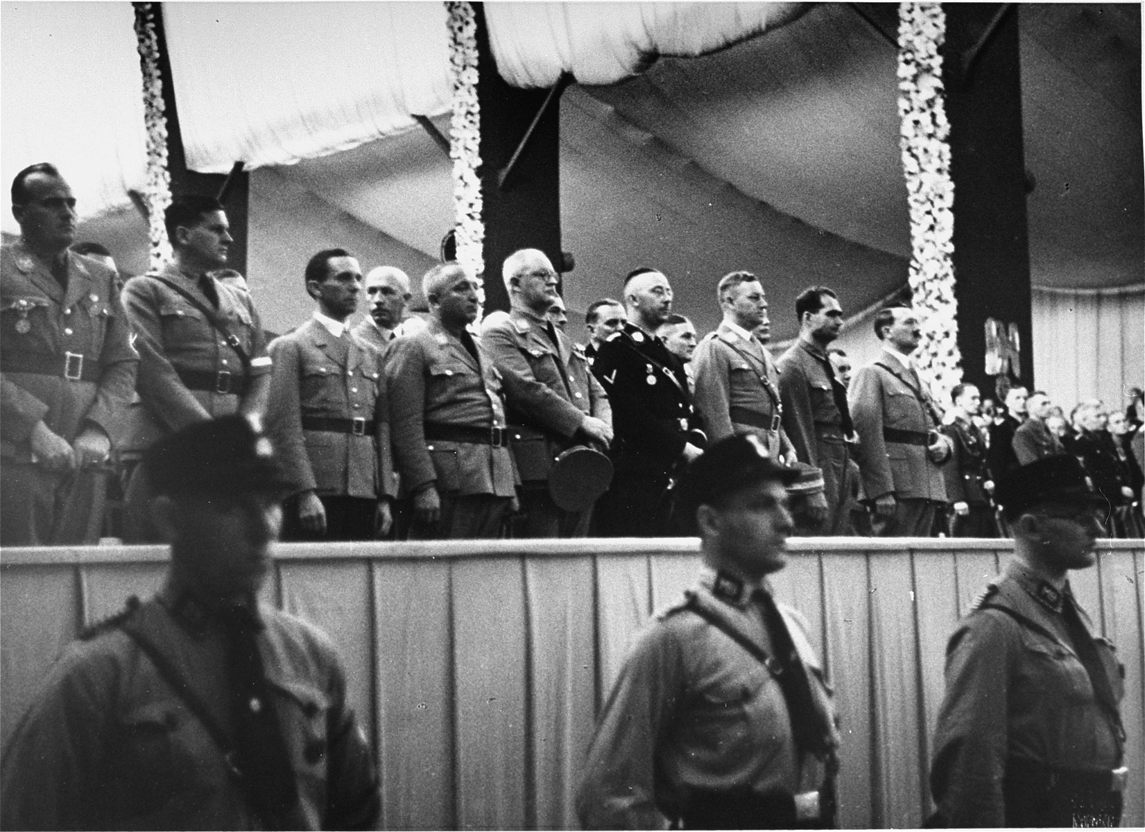 Adolf Hitler stands on a podium in the Luitpold Hall in Nuremberg with Rudolf Hess, Heinrich Himmler, and Joseph Goebbels during Reichsparteitag (Reich Party Day) ceremonies.  

This image is from an SS album.
