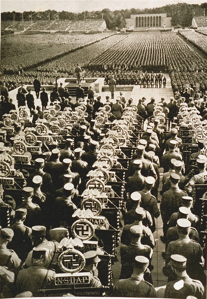 Adolf Hitler addresses the crowd assembled in the Luitpoldhain during Reichsparteitag (Reich Party Day) ceremonies.  

Behind him are standard bearers from various SA formations.