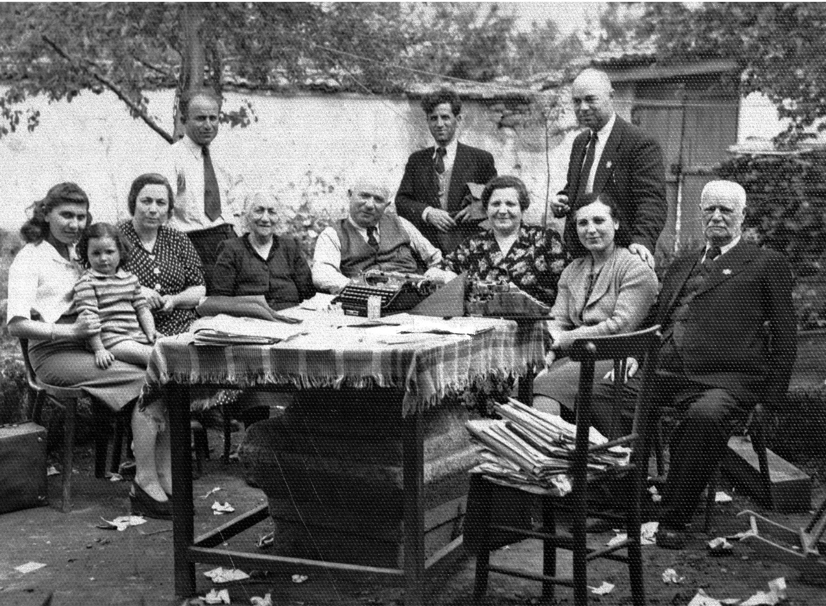 Members of the extended Baruch family pose outside around a table in the yard of their residence in Kyustendil, Bulgaria, following their expulsion from the capital, Sofia.

During the period of their exile in the provinces, the members of extended Baruch family lived in the home of Miriam and Pinkas Baruch, who had retained their house in Kyustendil after moving to Sofia in the 1930s.