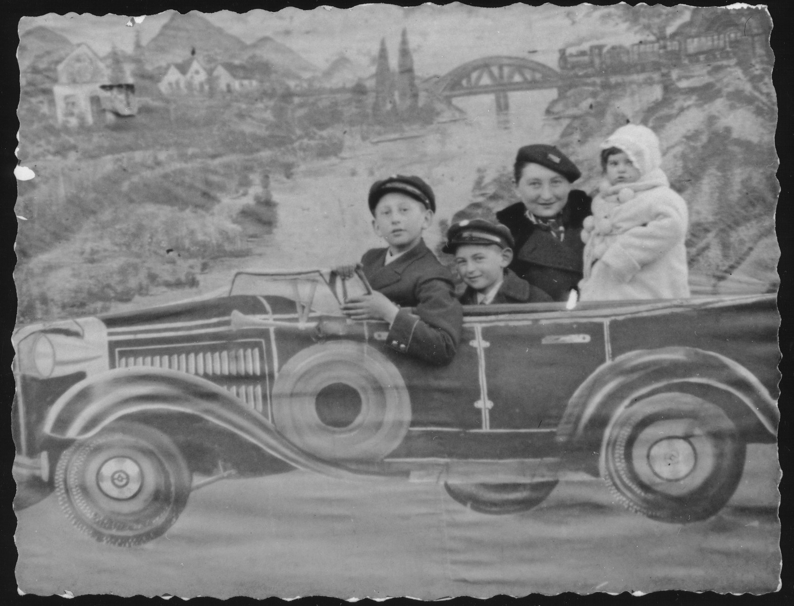 Zipporah (Katz) Sonenson poses with her younger brother and her two children against a backdrop of a sports car in the photo studio owned by her parents, Yitzhak and Alte Katz in Eisiskes.

Pictured from left to right are: Avigdor Katz, Yitzhak Uri Sonenson, Zipporah (Katz) Sonenson and Yaffa Sonenson.  After the paving of the Pilsudski Highway, to own or ride in a car became the aspiration of the younger generation in Eisiskes.  In the 1930s the sports car was the most popular backdrop in the Katz photography studio.  Avigdor Katz was killed by the Germans during the September 1941 mass shooting action in Eisiskes.