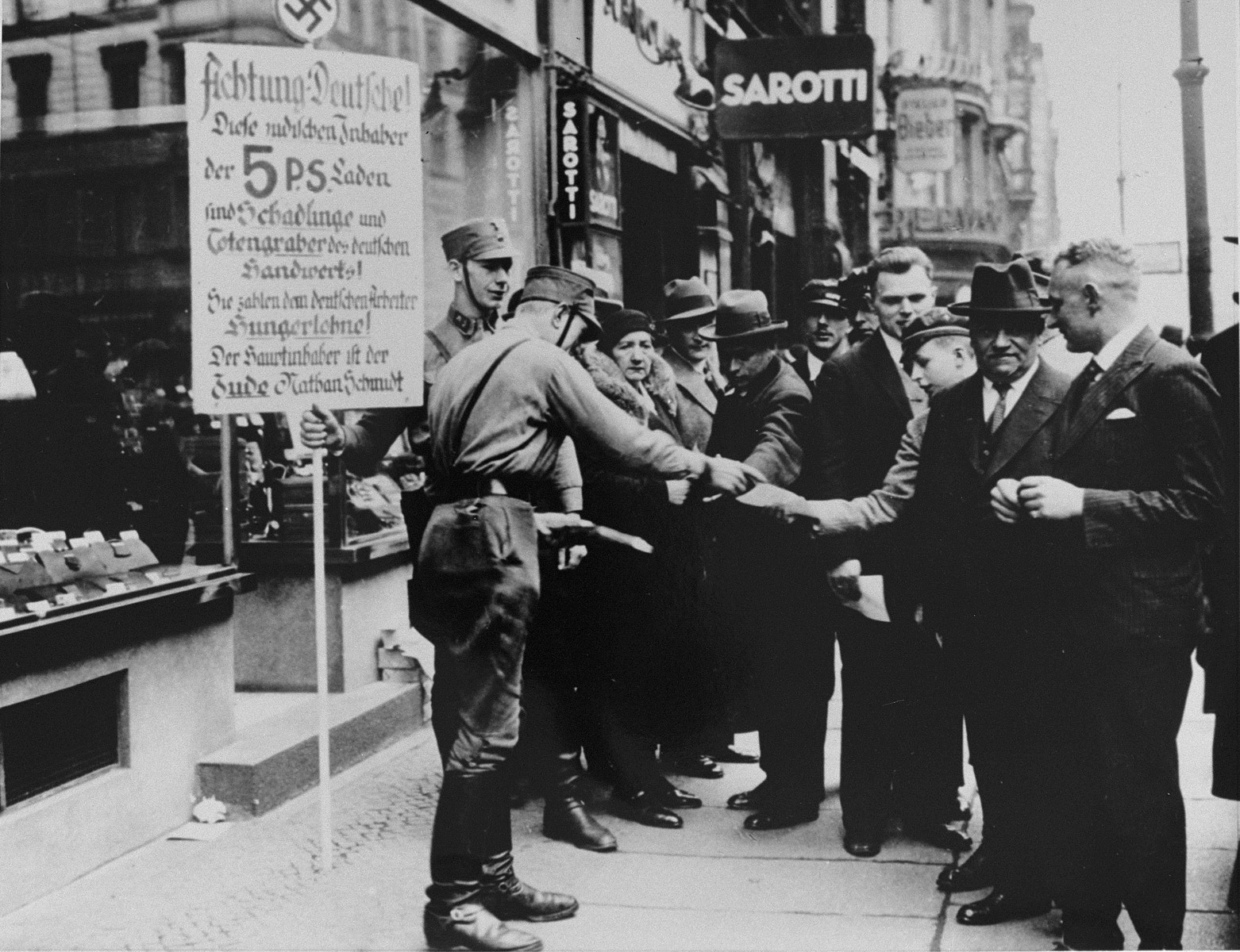 SA pickets distribute boycott pamphlets to German pedestrians.  The sign held by one of them reads: "Attention Germans. These Jewish owners of [five and dime] stores are the parasites and gravediggers of German craftsmen.  They pay starvation wages to German workers.  The chief owner is the Jew, Nathan Schmidt."