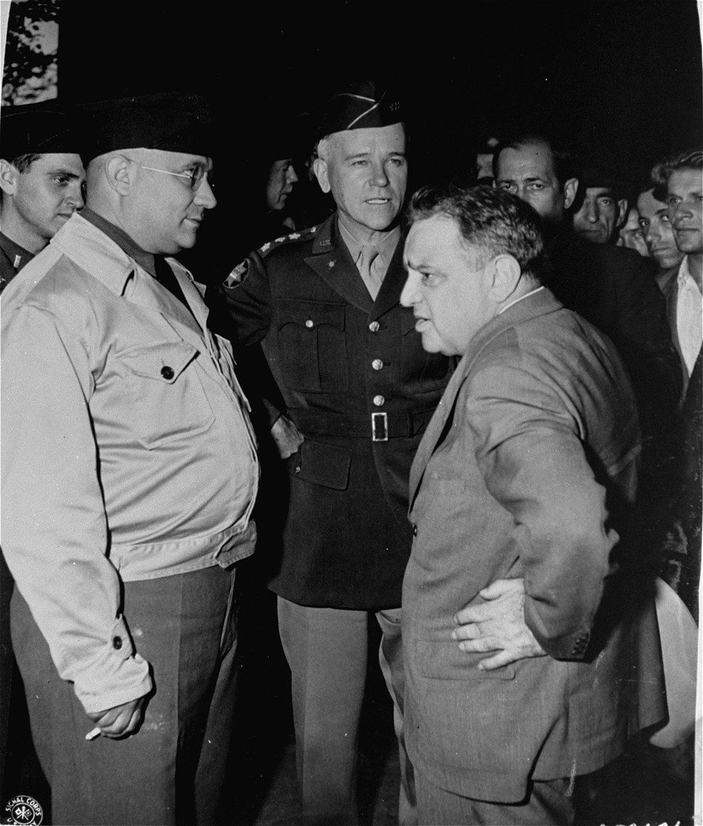 UNRRA Director General Fiorello LaGuardia speaks to General J. Lawton Collins (center) and UNRRA Schlachtensee camp director Harold Fishbein (left) during an official tour of the Schlachtensee displaced persons camp.

Also pictured in partially obscured on the left is Rabbi Mayer Abramowitz.