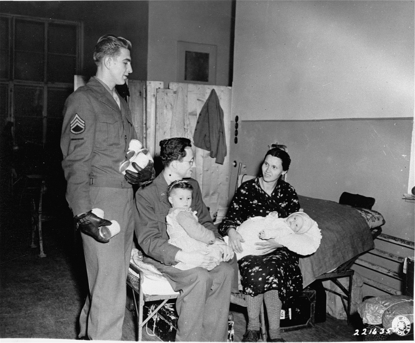 Sgt. Edward Bolshefski, of the Vienna Area Command, attached to the displaced persons' section (G-5), brings milk for Jewish DP children at a refugee center in Vienna. 

American Jewish Joint Distribution Committee field representative, James Rice, converses with the mother, while he holds one of her children in his lap.