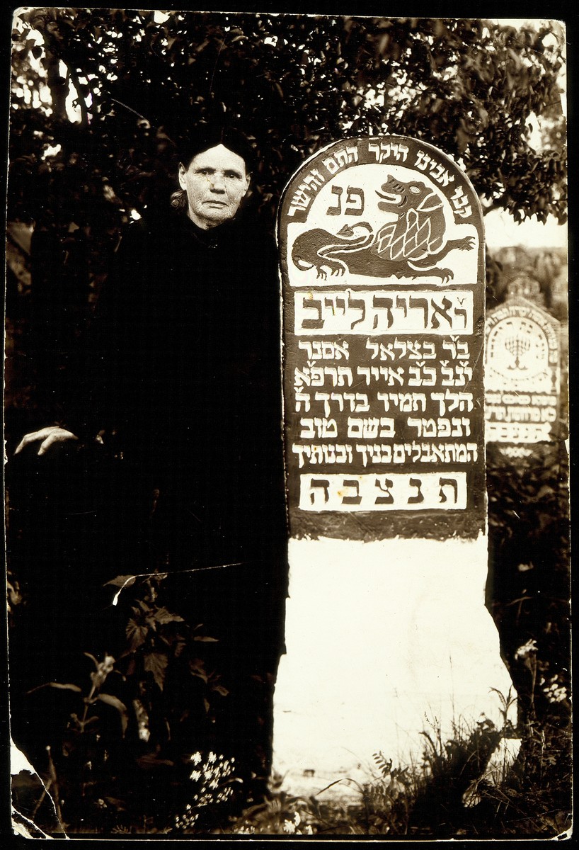 A woman poses next to the tombstone of Arieh Leib Asner.