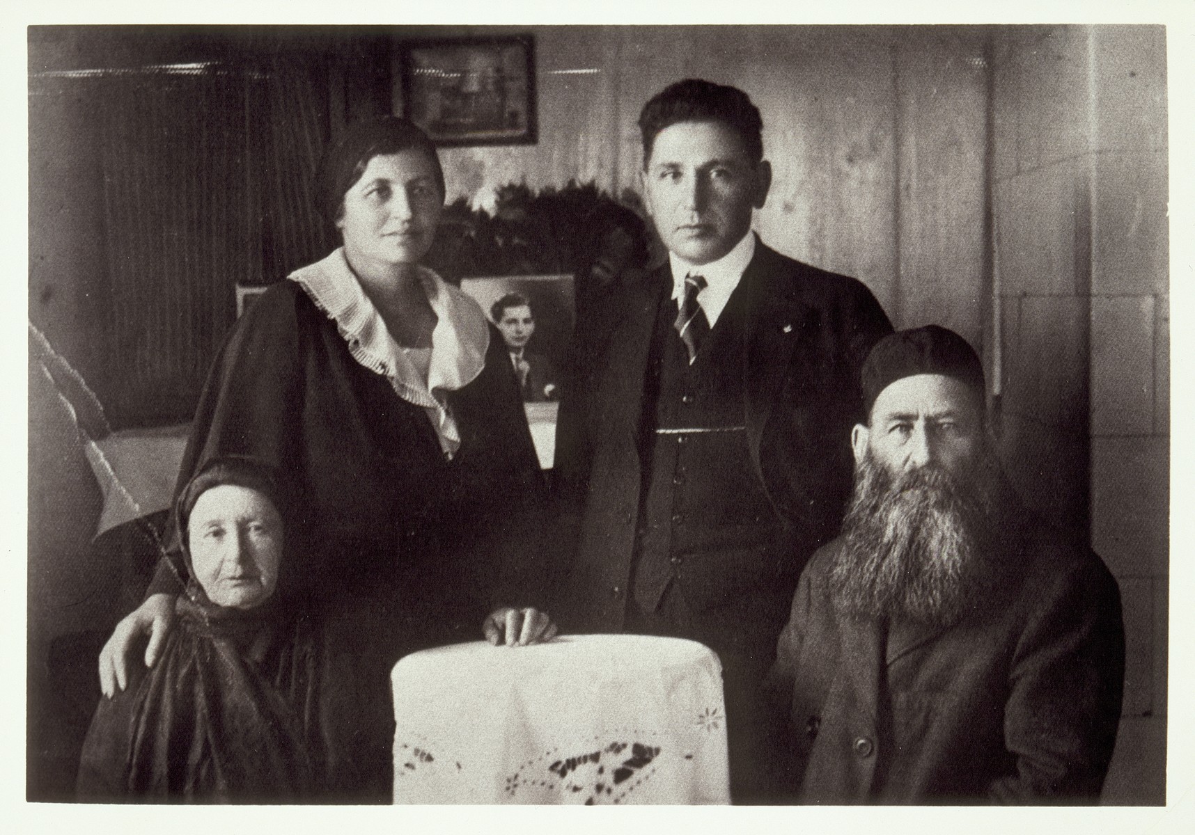 Esther Moszczenik and her husband Lou Gordon pay a visit from America to her elderly parents in Eisiskes. 

A picture of their son Milton is in the background.  Sitting is Reb Dovid "der Kirchier" Moszczenik and his wife Leah. Esther was their oldest daughter.  She lived in Boston, Mass.  Atara Zimmerman used to spend her summer vacatons with them at their house on the ocean.  Reb Dovid died a natural death.  His wife Leah was killed by the Germans during the September 1941 mass shooting action in Eisiskes.