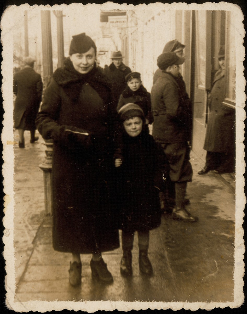 Ida Sonenson walks  down a street in a commercial district with her son Mulka (Meir) during the late 1930s.

Both were killed by the Germans during the September 1941 mass shooting action in Eisiskes.