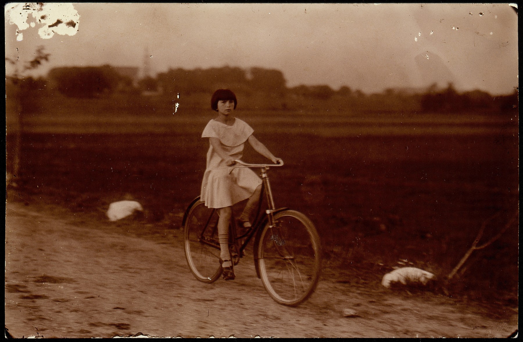 Atara Kudlanski rides a rented bicycle down a dirt road on the outskirts of Eisiskes. 

Her dress was a gift from her Aunt Sara in America.  In 1933 Atara joined her father in the United States.