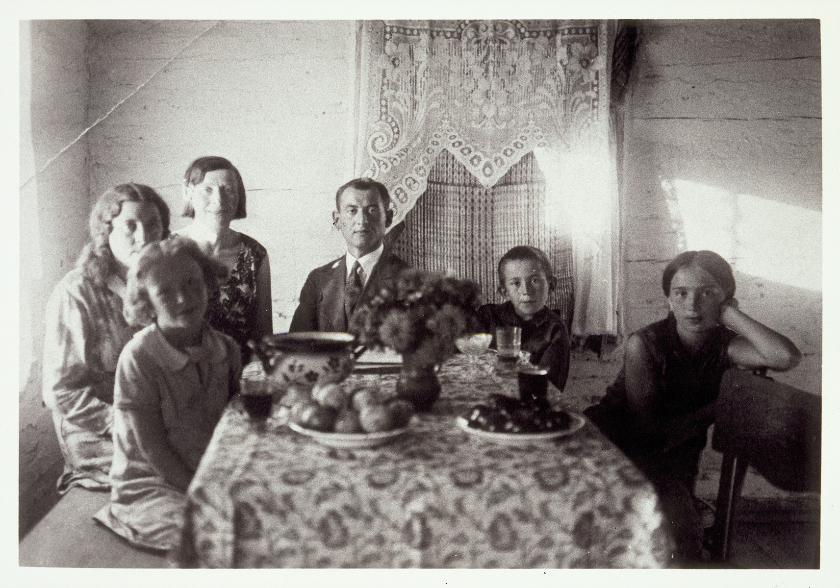 Dr. Zytoner, an assimilated Jewish veterinarian from Warsaw, sits in the center of a group of women and children around the Moszczenik dining room table. 

Dr. Zytoner boarded at the Moszczenik home while working in Eisiskes.  Pictured from right to left are Atara Kudlanski, her brother Bill, Dr. Zytoner, Atara and Bill's mother Hanneh-Beile  (nee Moszczenik), her sister Liebke, and her daughter Zltaka.  

Hanneh-Beile and her three children immigrated to America.  Liebke was killed by the Polish Home Army.