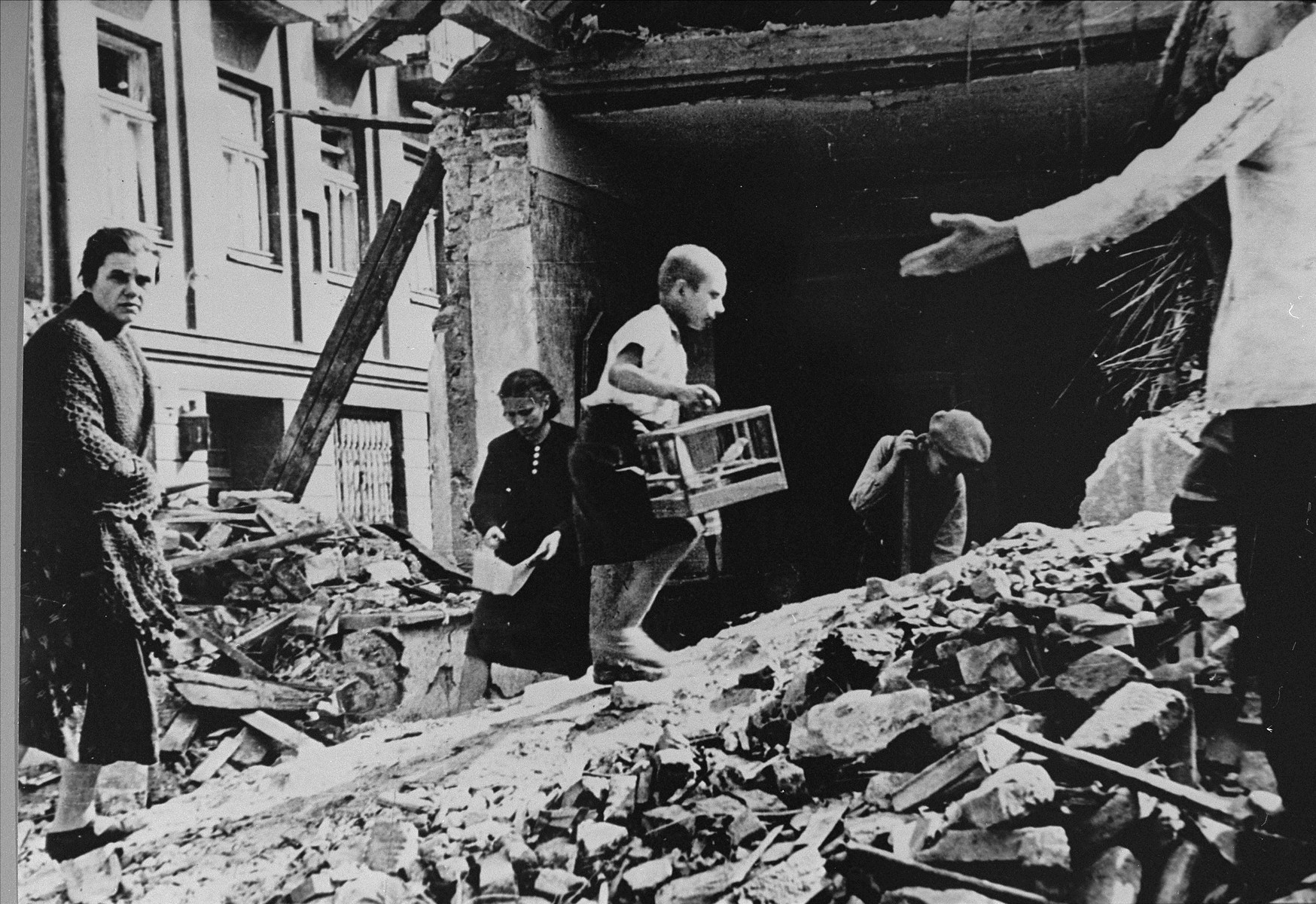 Polish civilians salvage items from the ruins of their homes in Warsaw after a German air raid. 

The child carrying the birdcage is Zygmunt Askienow.

In the words of photographer Julien Bryan, "Not far from the center of town a bomb had hit an apartment house and exposed the first, second, and third floors.  A boy was walking dazedly back and forth carrying the one possession he had found -- a canary in its cage.  He walked up and down over a pile of stones and bricks.  Under the pile there were nine or ten bodies, so the neighbors told us, not yet recovered." [Source: Bryan, Julien.  "Warsaw 1939 Siege, 1959 Warsaw Revisited."  Warsaw, Polonia, 1959, p. 24]