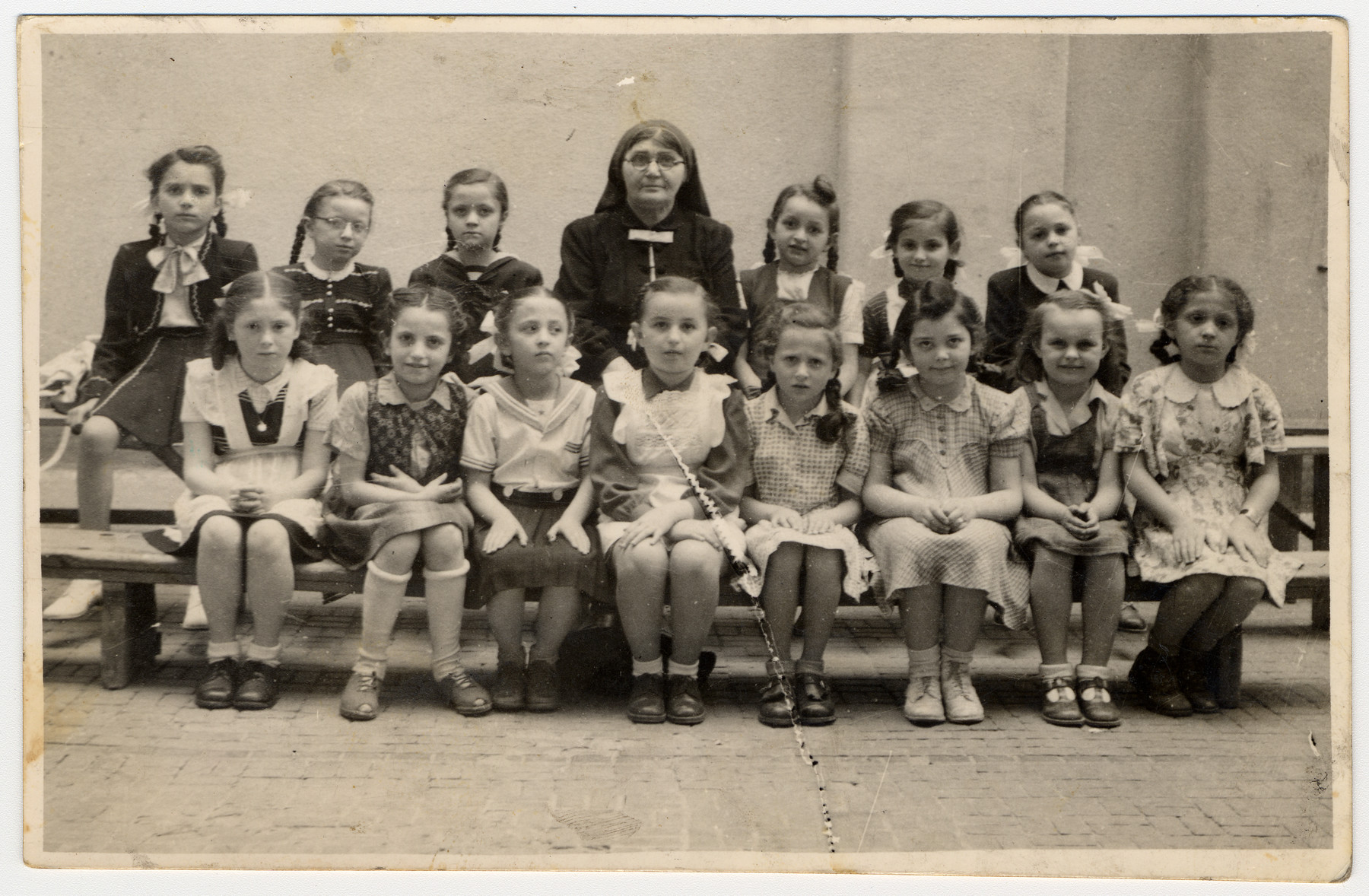 Group portrait of girls in an Orthodox Jewish elementary school in Budapest.

Among those pictured is Zsuzsa Rubin in the back row to the right of the teacher.