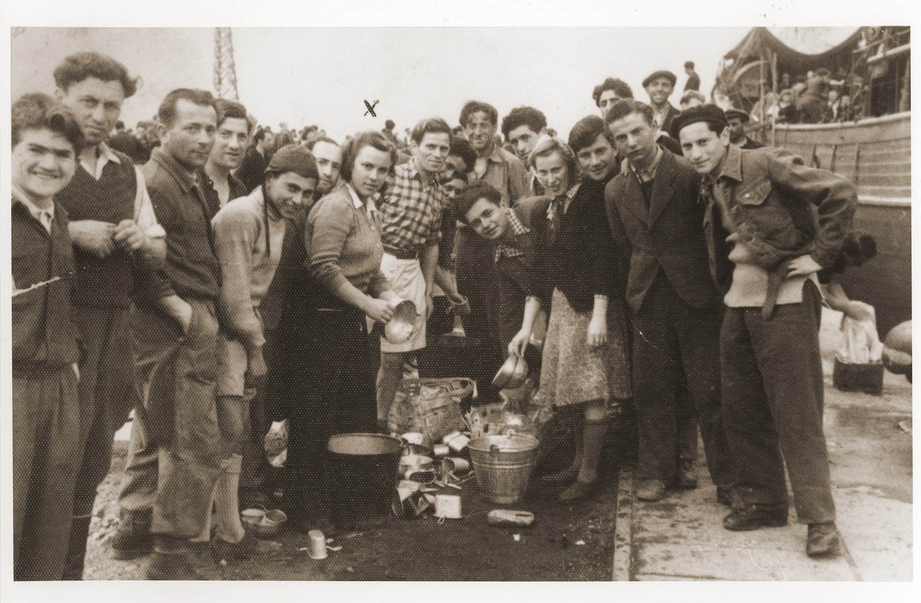 Group portrait of Jewish DPs on the pier in the port of La Spezia, where they await permission to sail to Palestine.  

Saba Fiszman is in the center holding a pot.  She drew an 'x' over herself to identify herself to her brother who had not seen her in eight years.