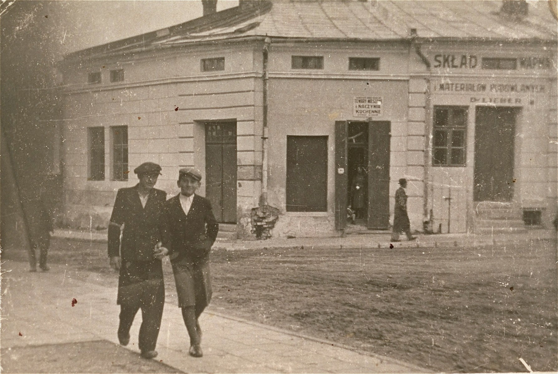 Two friends walk along a street in the Kolbuszowa ghetto.

Pictured is Manius Notowicz (right) with a friend named Grinstein in front of Lieber's building supply store.