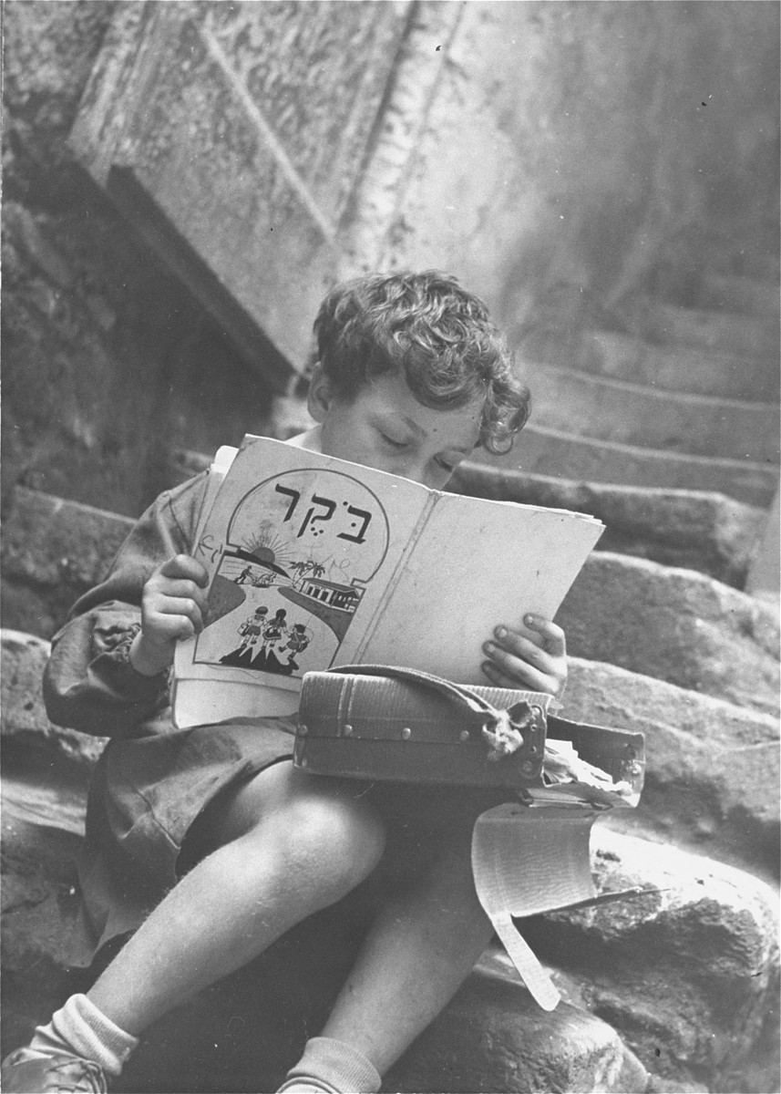 A young Jewish boy studies his Hebrew reading book on the steps of his house in the old Jewish quarter of Rome.