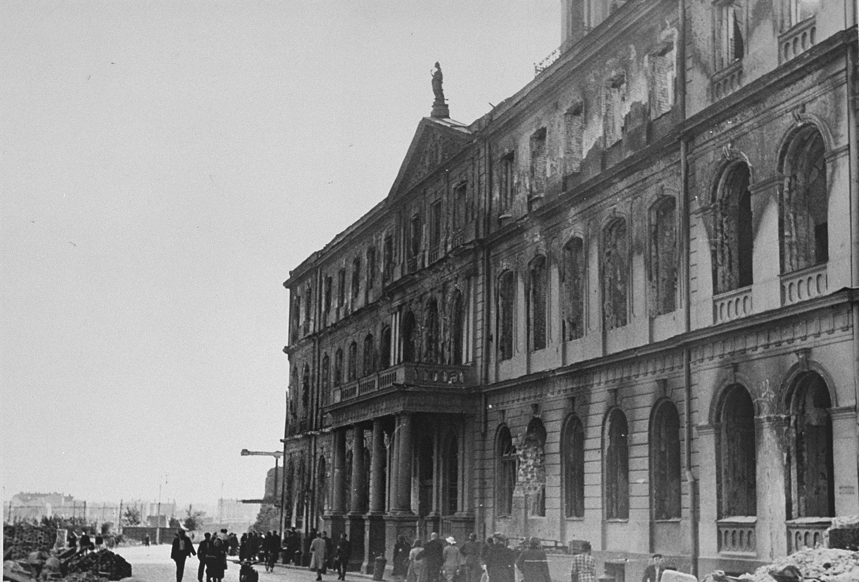 Latvian civilians walk past the Riga city hall, which was damaged in a German air raid.