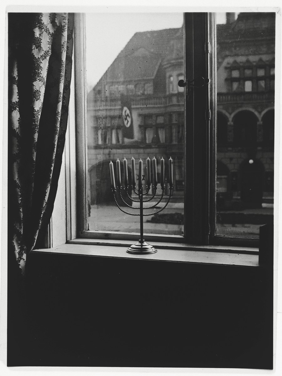 A Hanukkah menorah rests on the sill of an apartment window in Kiel.  

The window looks out on the town hall, in front of which a Nazi banner hangs.  The menorah belonged to Rabbi Akiva Posner, the rabbi of Kiel.