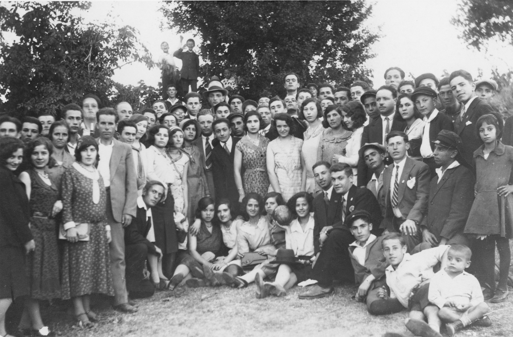 A group of Macedonian Jewish young men women and children pose together outside.