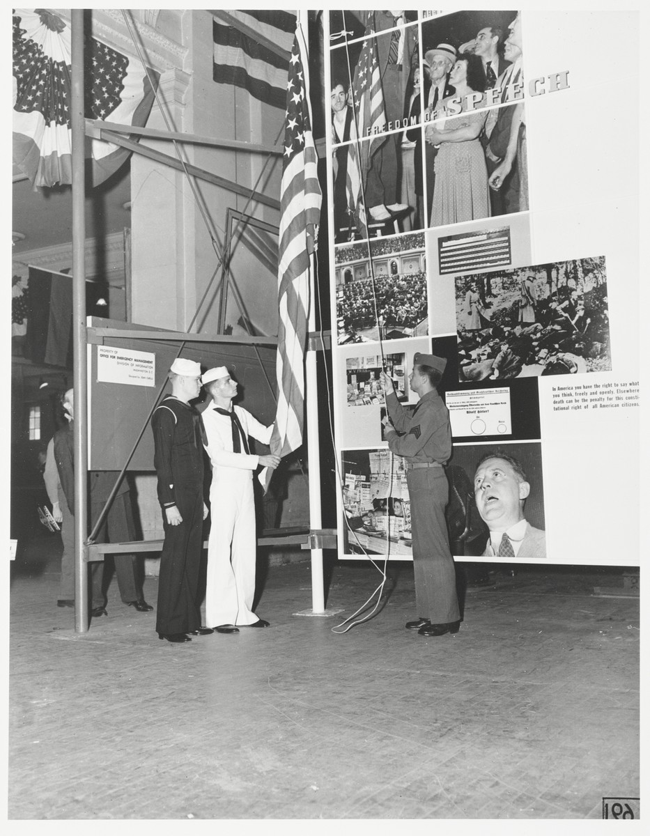 Old Glory raised before the Four Freedoms exhibit.

Designers, painters, printmakers, writers, sloganeers, and poster artists created stamps, billboards, pamphlets, woodcuts, prints, murals, and even a sculpture -- at Roosevelt's request -- to bring the President's message to a broad public.  A month before Pearl Harbor, the Office of Emergency Management commissioned Jean Carlu to mount an exhibit, a photomontage that traveled to scores of American cities explaining during the war years "why we fight."