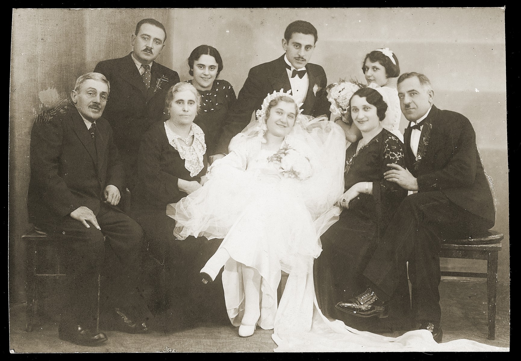 Group portrait of family members at the wedding of Mosa (Moshe) Mandil and Gabriela (Ela) Konfino in Belgrade.  

Pictured are Mosa Mandil and Gabriela Konfino, the groom and bride, David and Regina Mandil, the groom's parents (seated on the left); Gavra and Elisabeth Konfino, the bride's parents (seated on the right); Streja Mandil, the groom's sister, and her husband (standing on the left); and Gizela Konfino, the bride's sister (standing on the right).