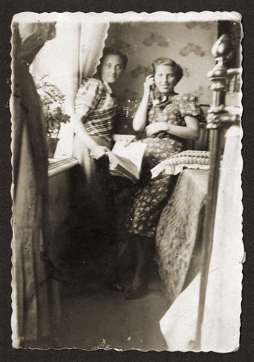 Two young Jewish women, one of whom is talking on the phone, sit in a private home in Opatow, Poland.

Pictured is Sylka (Fefer) Sztajman (right) with her sister-in-law, Fela Sztajman (left) in Fela's home.