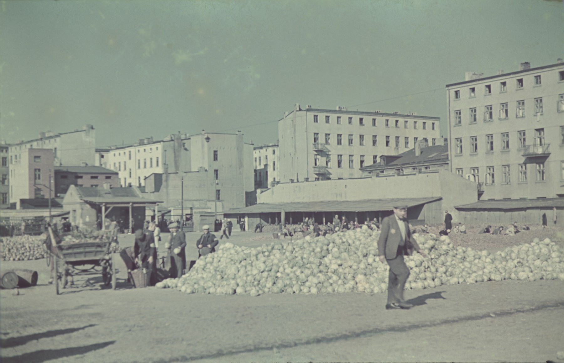 A man walks past a past a pile of vegetables in the Lodz ghetto central square.

Original German caption: "Lagerplatz" (camp square), #144.