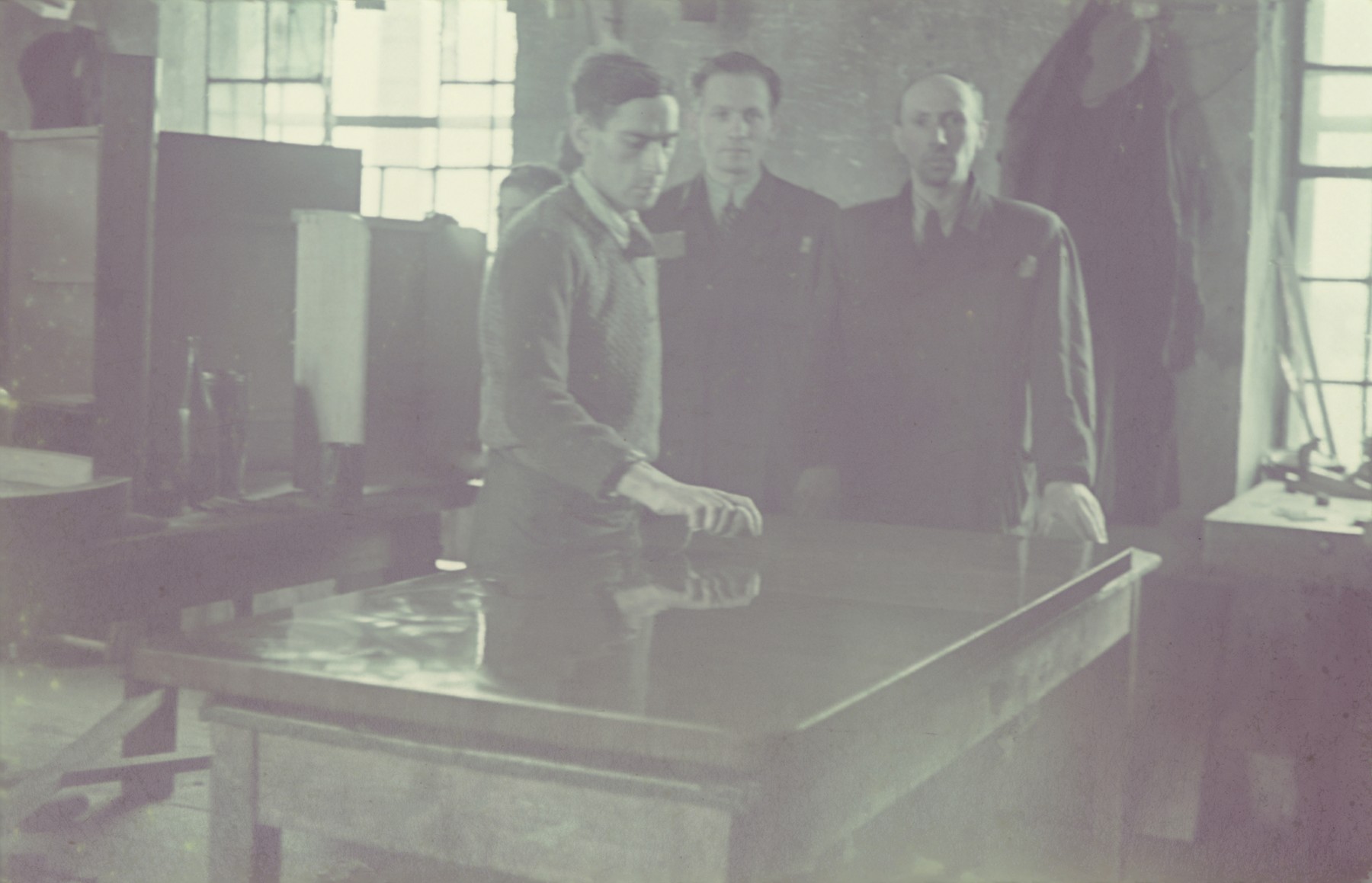 Three men examine the finish of a table in the furniture factory of the Lodz ghetto.

Original German caption: "Getto-Litzmannstqadt, Moebelfabrik" (furniture factory), 1942, #12.