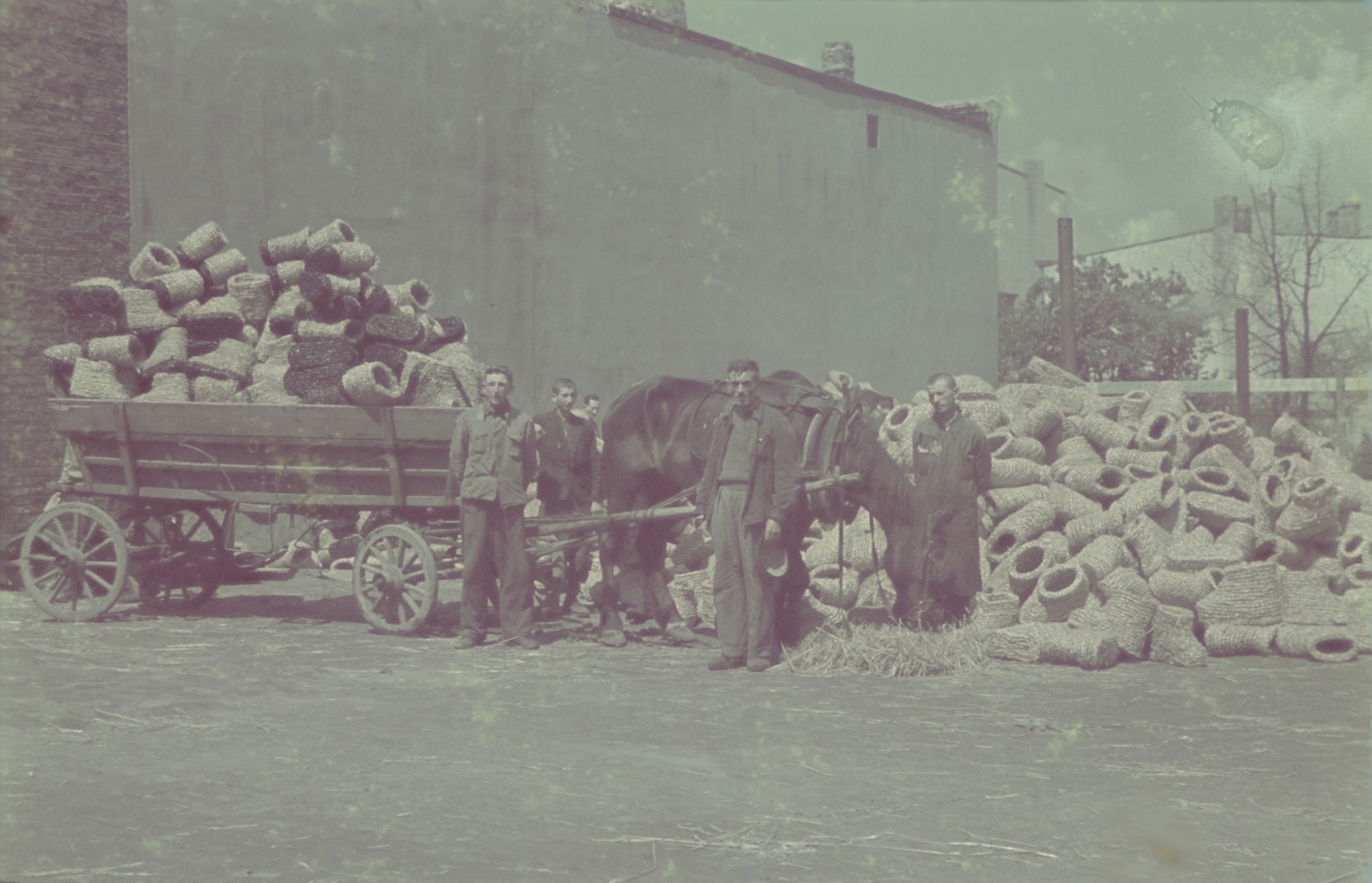 Workers pile coils of straw onto a horse-drawn cart outside the factory for straw shoes in the Lodz ghetto.

Original German caption: "Getto Litzmannstadt, Strohschuhfabrik" (straw shoe factory), #205.