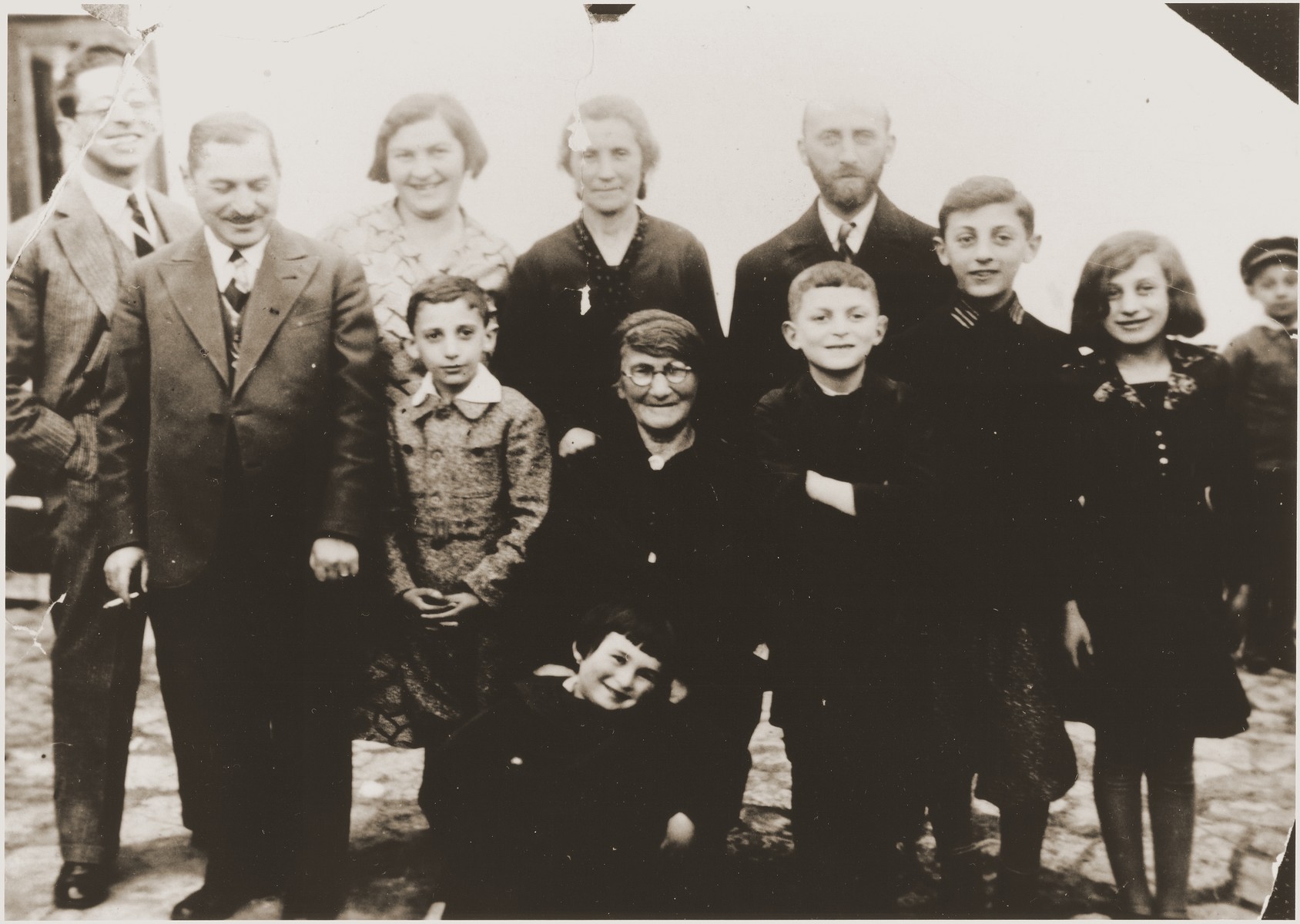 Group portrait of the extended Jewish Hochberg family in Brody, Poland. 

Pictured in the back from left to right, are: Marco Chaim Lifschitz-Hochberg (the donor's uncle); Bernard Hochberg (the donor's father); Dina (Harmelin) Hochberg (the donor's mother); Malka (Hochberg) Katz (the donor's aunt); and Efraim Katz (the donor's uncle). In the middle from left to right, are: Abraham Katz (the donor's cousin); Batja (Lifschitz) Hochberg (the donor's grandmother); Sigmund Hochberg (the donor's brother); Itamar and Rachel Katz. In front is the donor, Eugenia Hochberg.