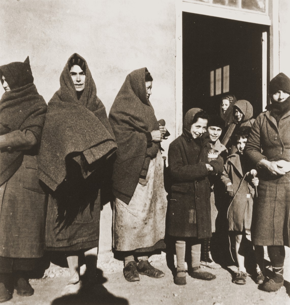 Women and children try to stay warm while waiting for food distribution.