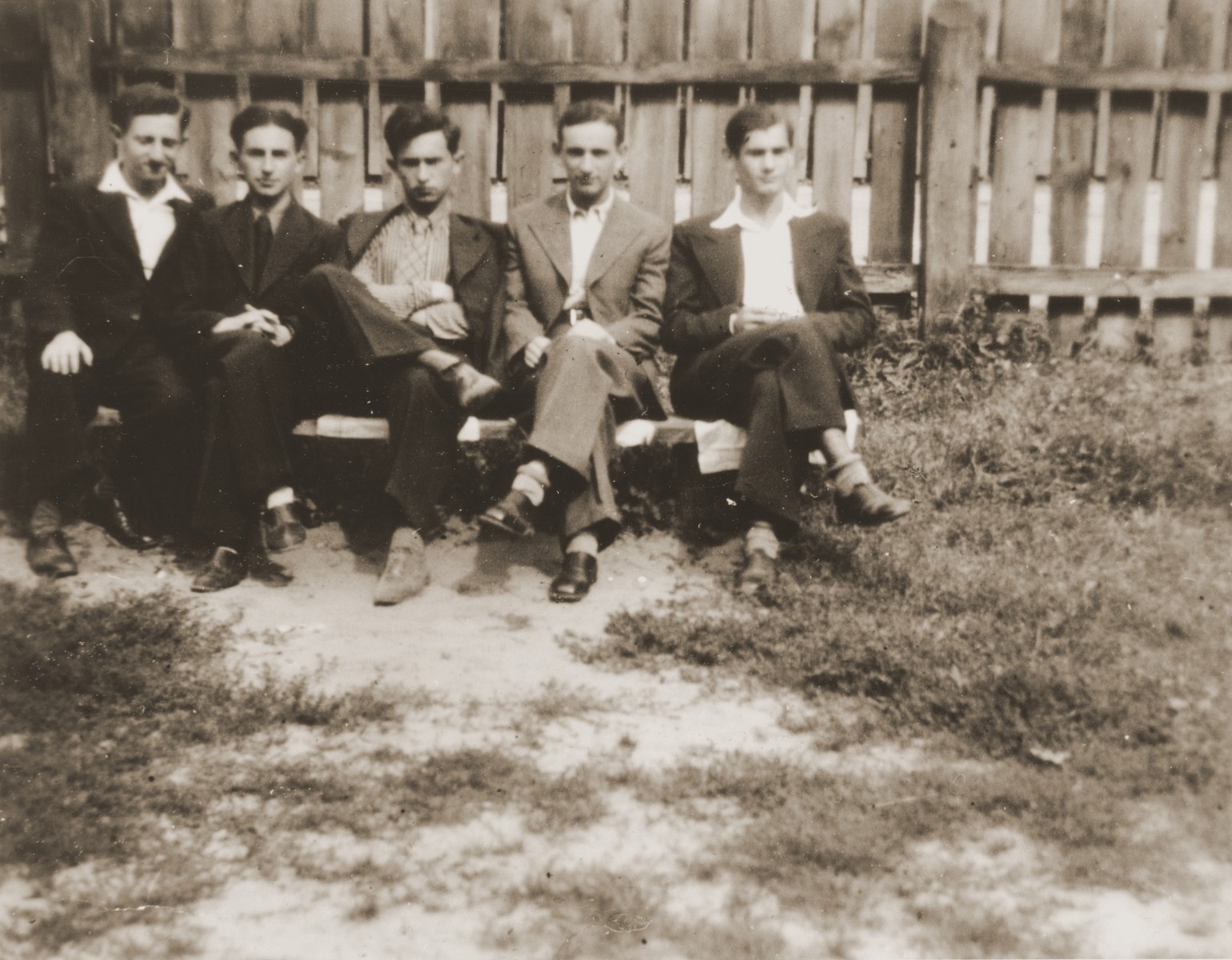 Five Jewish high school friends pose outside on a bench in front of a fence in Brody, Poland.  

Among those pictured are: Joseph Ettinger (right) and Henryk Lanceter (second from the right).