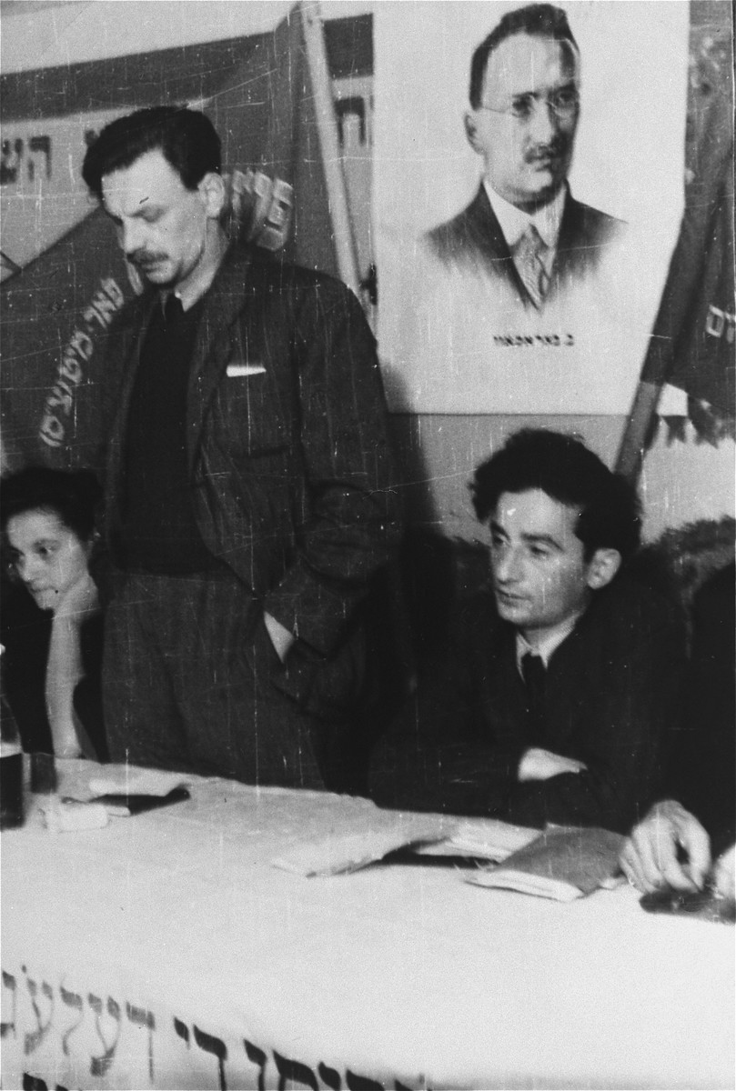 Yitzhak Zuckerman delivers a speech at a Zionist meeting in Zeilsheim.  A portrait of the socialist Zionist theorist Ber Borochov hangs behind the speaker.