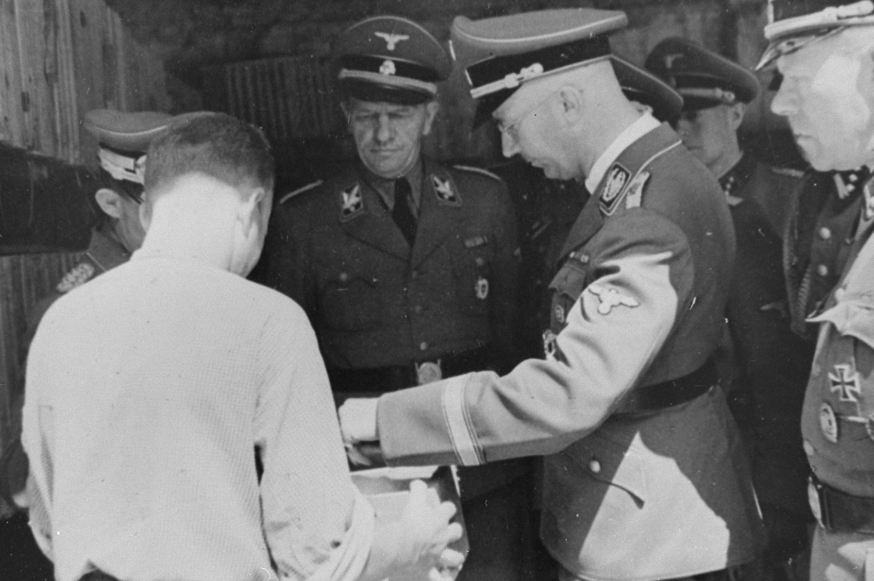 Reichsfuehrer SS Heinrich Himmler examines the contents of a box during an inspection tour of the Monowitz-Buna building site.   

Pictured on the far right is Himmler's bodyguard, SS Hauptsturmfuehrer Josef Kiermaier.  In the center is SS-Gruppenfuehrer Hanns Johst.
