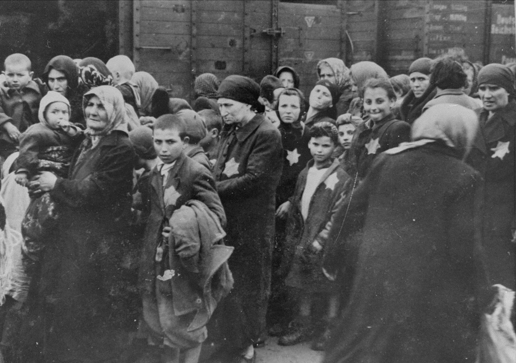 Jewish women and children from Subcarpathian Rus await selection on the ramp at Auschwitz-Birkenau.

Pictured at the left is Rosa Goldenzeil holding her grandson Dani Jakubovitch.  On the right is Armin Riter who had accompanied his mother and sisters to the women's side before rejoining his brothers and father on the men's side.