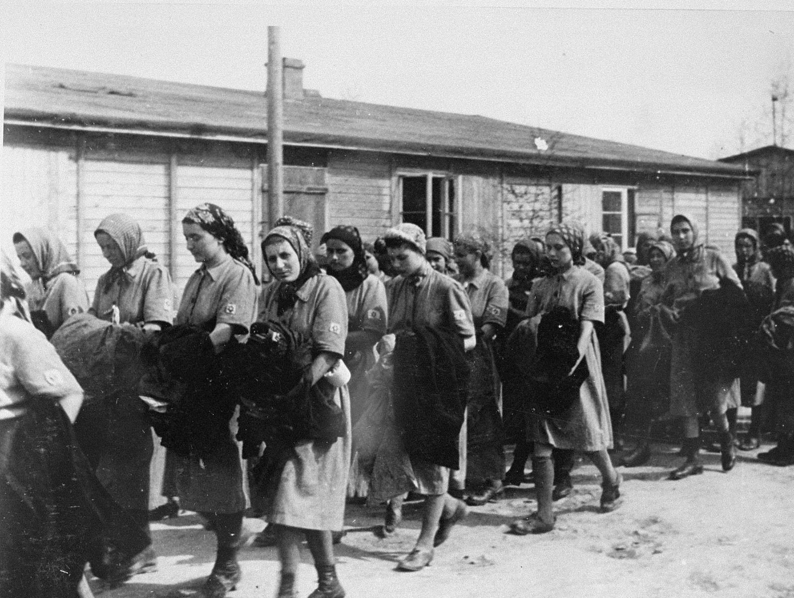Jewish women from Subcarpathian Rus who have been selected for forced labor at Auschwitz-Birkenau, march toward their barracks after disinfection and headshaving.

Among those pictured from left to right are Martha Birnbaum Younger, Dora Birnbaum, Erna Birnbaum Gottesman, Gina Liebermann or Etush Zelmanovic (later Esther Moses),  Agi Katz Rubin, and Mignon Gottesman (now Bretzholz), Maidi Birnbaum and Rozi Feldman.