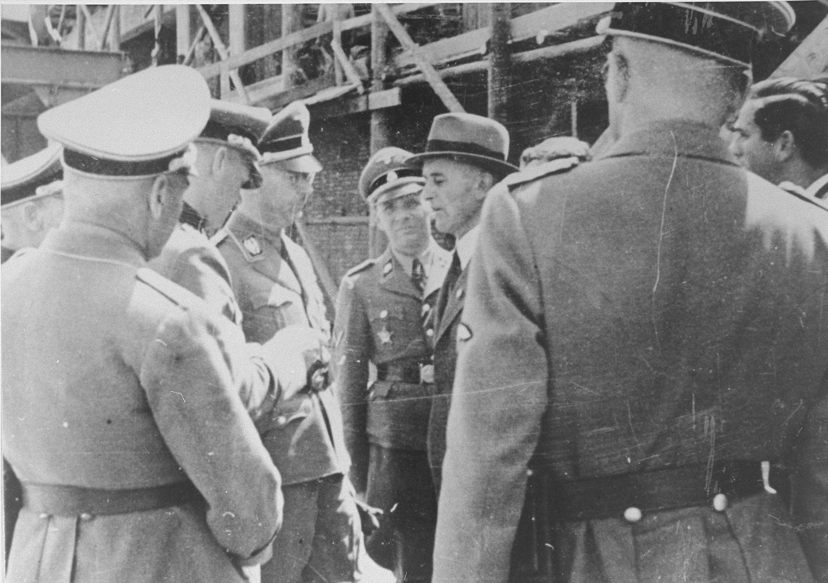 Officials at the Monowitz-Buna building site greet Reichsfuehrer SS Heinrich Himmler and his inspection team.   

Among those pictured are Max Faust (wearing the fedora), the head of building operations for IG Farben in Monowitz-Buna; and Heinrich Himmler (third from the left).  Facign the camera (fourth from the left) is Rudolf Hoess, Commandant of Auschwitz.