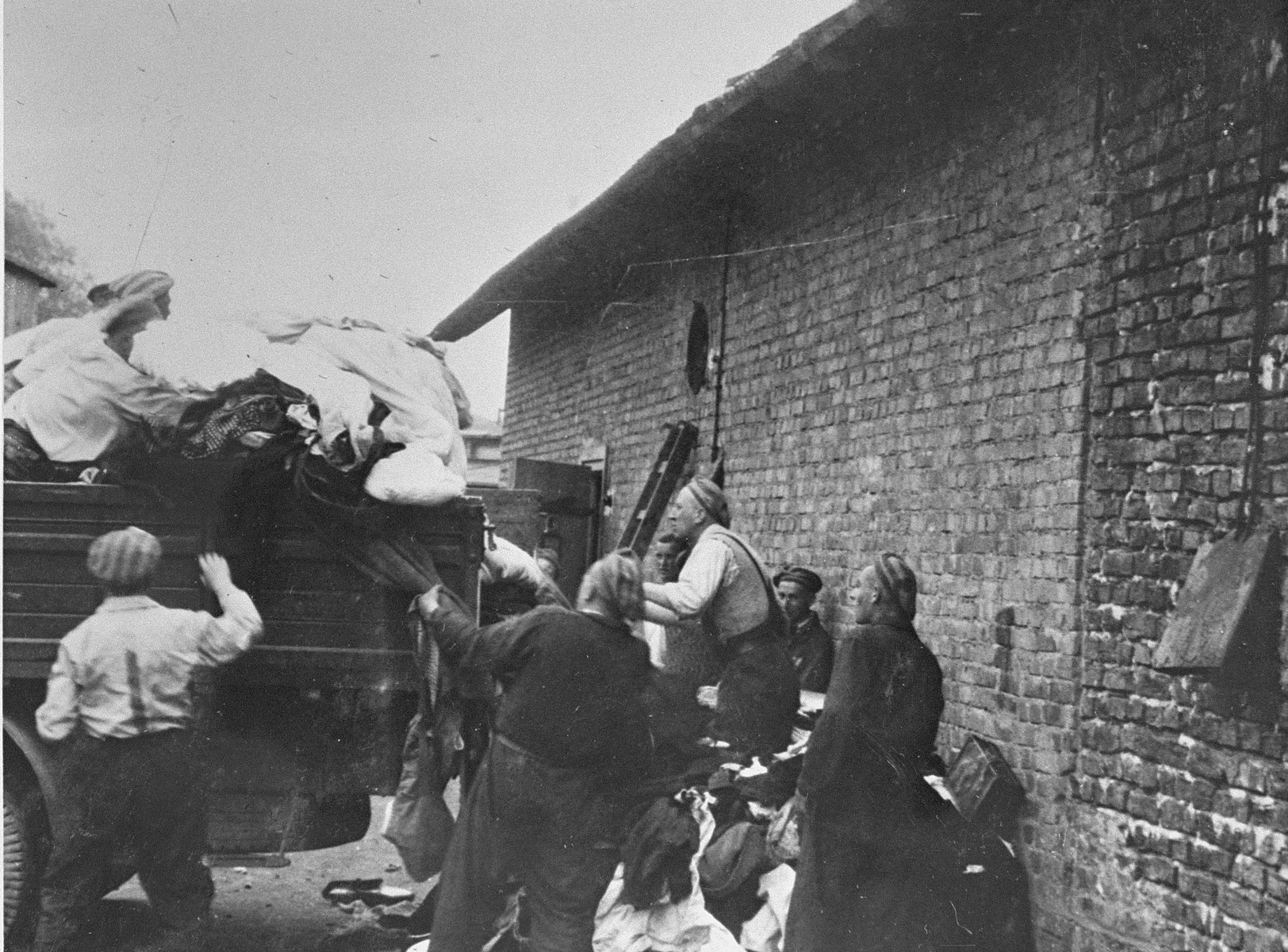 Prisoners in the Aufräumungskommando (order commandos) unload the confiscated property of a transport of Jews from Subcarpathian Rus at a warehouse in Auschwitz-Birkenau.

The camp prisoners came to refer to the looted property as "Kanada," associating it with the riches symbolized by Kanada.  The members of this commando were almost exclusively Jews.  "Kanada" storage facilities occupied several dozen barracks and other buildings around the camp.  The looted property was funneled from Auschwitz through an extensive distribution network that served many individuals and various economic branches of the Third Reich.

Standing from left to right are Simon Bobker, Alexander Wertheimer. Chaim Laufer and Miso Vogel.