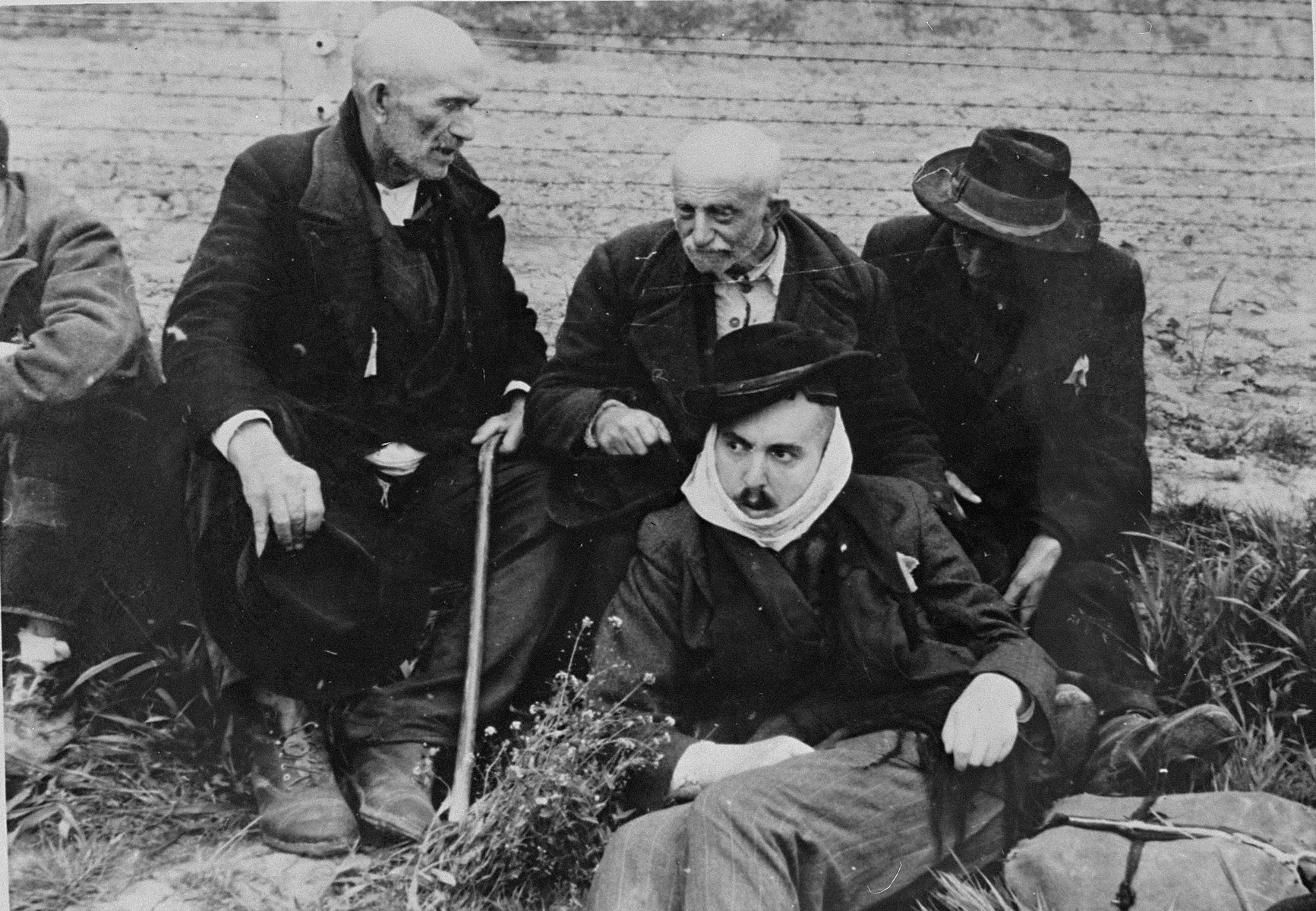 Elderly Jewish men from Subcarpathian Rus sit on the grass in Auschwitz-Birkenau prior to being sent to the gas chambers.

One of the men wears a scarf to cover his shaven face.