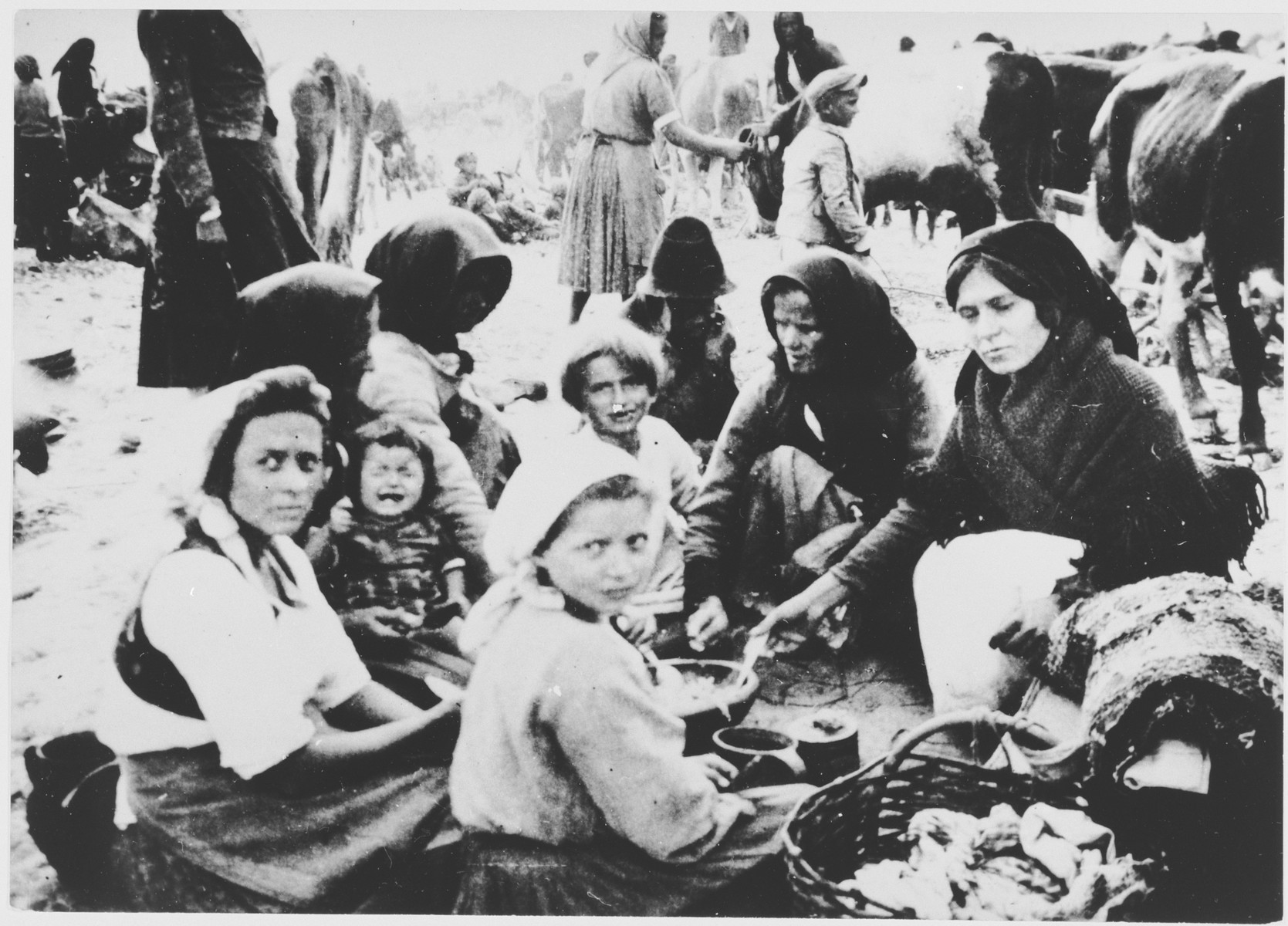 [Probably Serbian women and children from the Kozara region who have been rounded-up for deportation, eating a meal outside at a transit camp.]