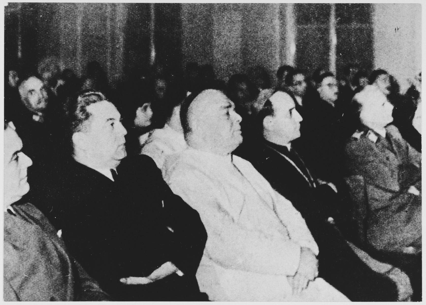 Croatian political and religious leaders sit in the audience at an unidentified ceremonial gathering.

Pictured in the front row from left to right are: Minister of the Interior Andrija Artukovic (second from the left in the dark suit), Papal legate Giuseppe Ramiro Marcone, and Archbishop Alojzije Stepinac.