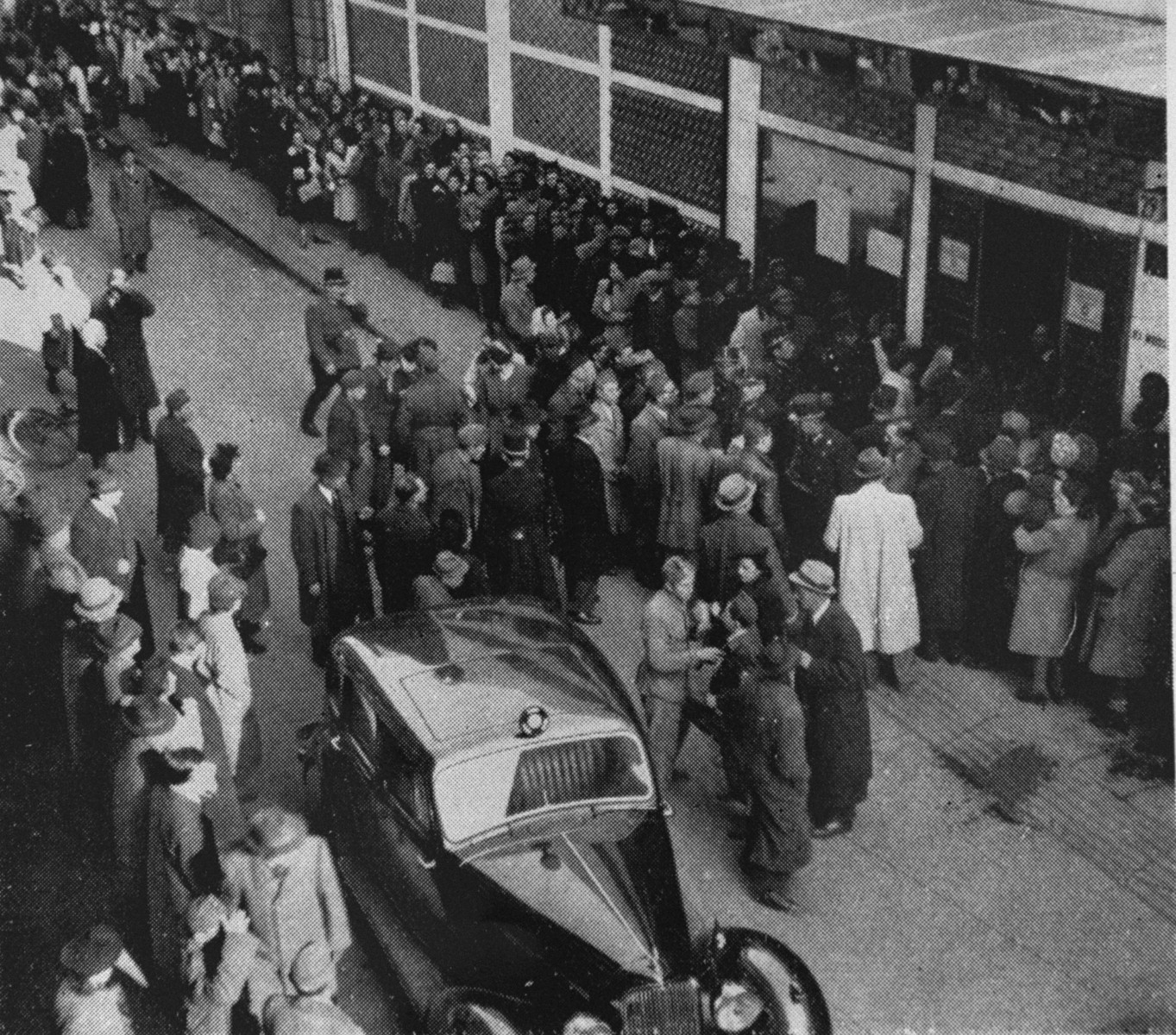 Police attempt to control the crowd of Jews, who are waiting outside a branch of the Swiss legation located in the Glass House on Vadasz Street hoping to obtain Schutzbriefe that would protect them from deportation.

In the foreground is the car used by Vice Consul Carl Lutz.