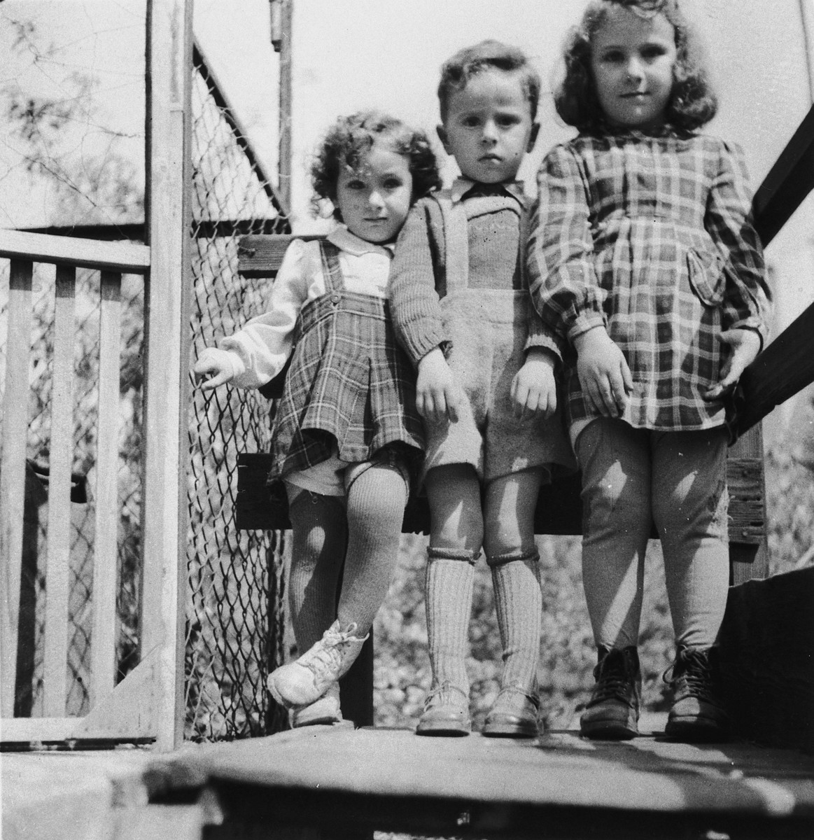 Three young children pose outside next to a fence in the Wasseralfingen DP camp.

Pictured are Pauline, Joseph and Rita Slepian.