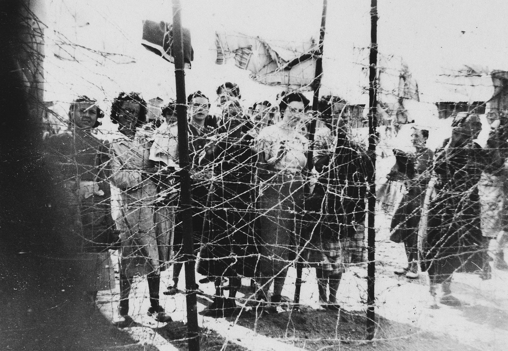 Female prisoners gather by the barbed wire fence surrounding the Gurs concentration camp in France.