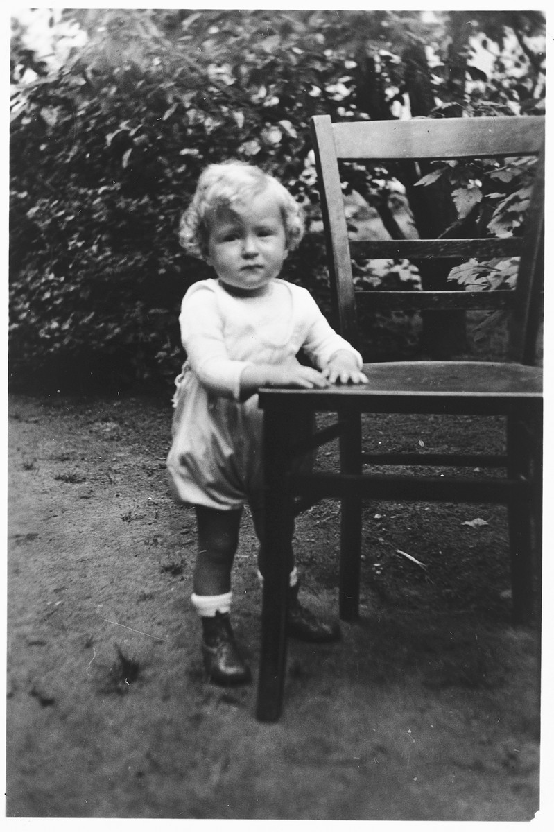 Portrait of a Jewish toddler holding onto a chair in the garden of a home in Frankfurt am Main, Germany.

Pictured is one-year-old Brigitte Joseph.